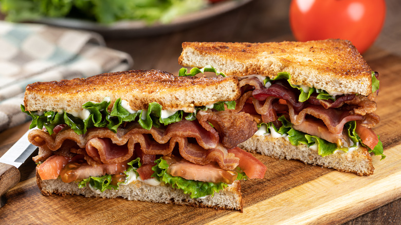 A BLT sandwich sliced in half and sitting on a wooden cutting board