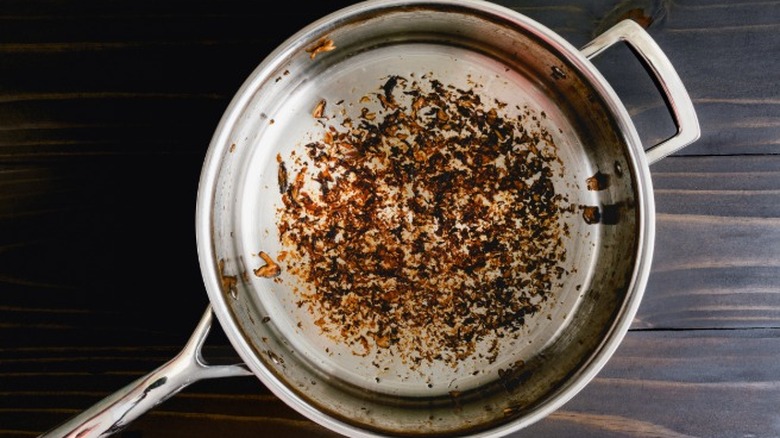 Food remnants stuck to the bottom of a stainless steel pan that needs to be deglazed.