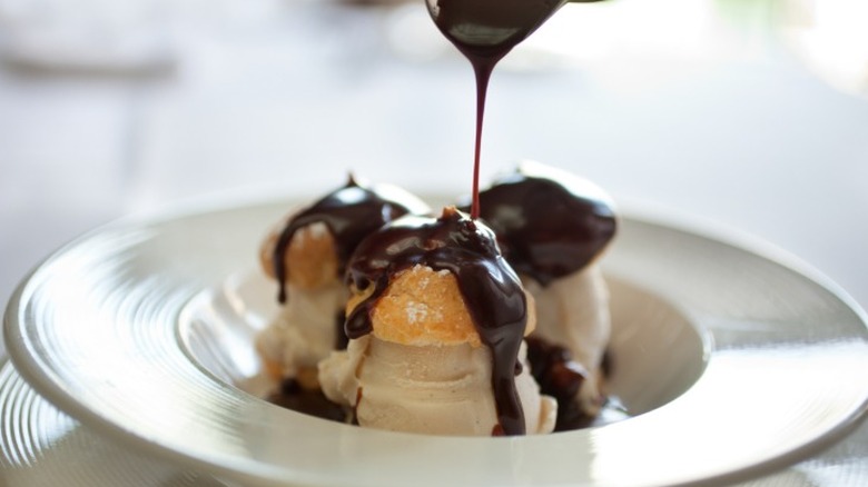 A dark chocolate sauce with whiskey in it being drizzled over a cream puff dessert.