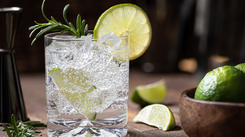 Club soda with lime and a rosemary sprig next to cut limes and a jigger in the background