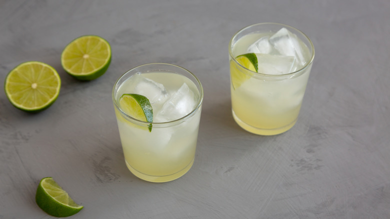 Two glasses of limeade garnished with lime wedges, next to a halved lime