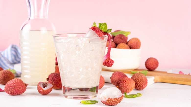 Cup of lychee juice with lychee fruit next to a pitcher of lychee juice in the background