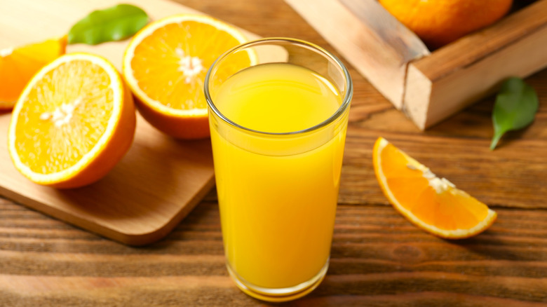 A glass of orange juice next to halved oranges on a cutting board
