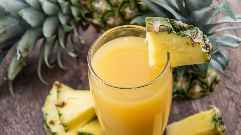 A glass of pineapple juice garnished with a pineapple quarter slice and a whole pineapple in the background
