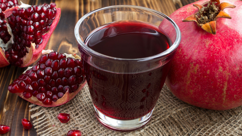 A glass of pomegranate juice next to a whole pomegranate and a chunk of the fruit showing the arils inside