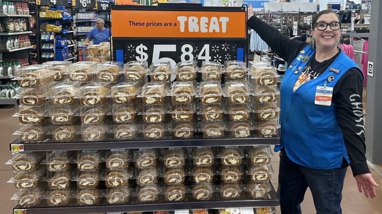 Walmart employee standing next to stacks of pumpkin cake rolls