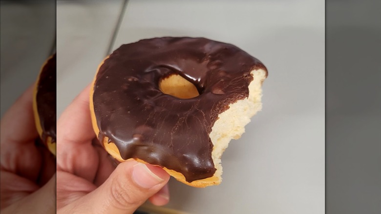 Person holding a chocolate frosted donut with a few bites taken out of it