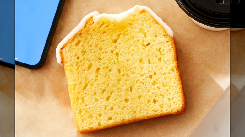 A slice of Marketside Iced Lemon Loaf Cake on a wooden table next to a cell phone