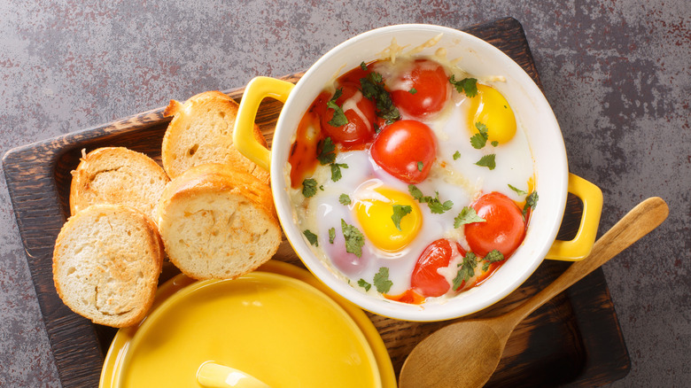 Shirred eggs with tomatoes and herbs, next to toast