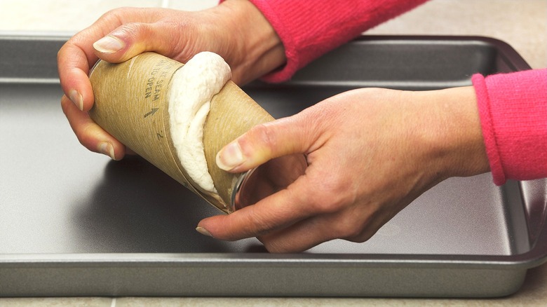 Hands opening a can of refrigerated dough over a metal sheet pan