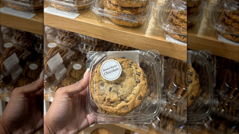 Person's hand holding a plastic clamshell container with a brown butter chocolate chunk cookie