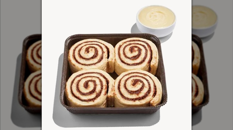 Four uncooked Whole Foods cinnamon rolls next to a bowl of cream cheese icing