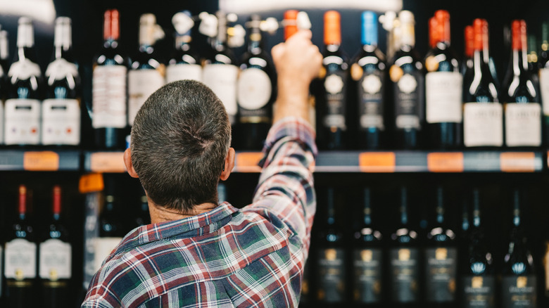 A man reaching for a bottle of wine in a store.