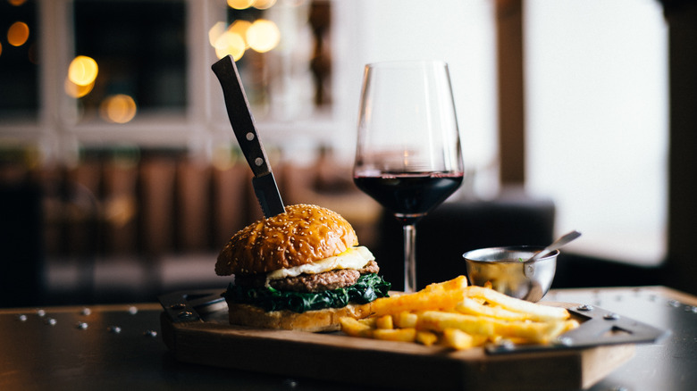 A glass of red wine next to a burger.