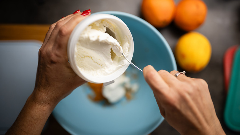 Hands using spoon to scoop ricotta from container