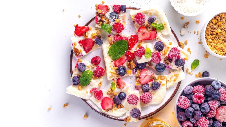 Pieces of frozen yogurt bark covered in berries and mint leaves on a white plate