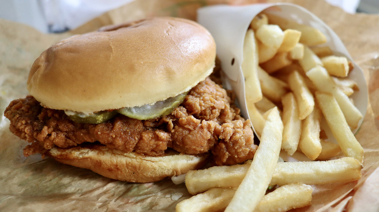 Unbranded crispy chicken sandwich and french fries on paper wrapper.