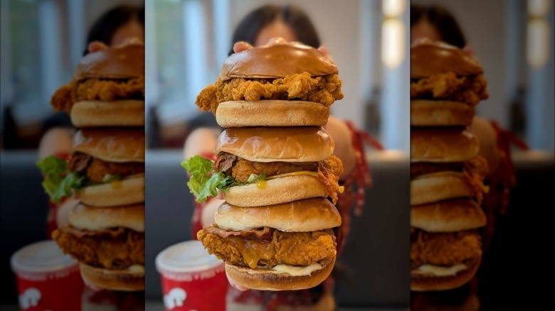 Woman holding three Jollibee chicken sandwiches on top of one another in restaurant.
