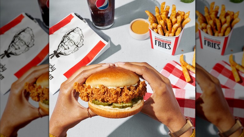 Woman holding KFC crispy chicken sandwich next to soda and french fries.