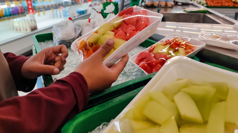 A person holding a pack of sliced melons.