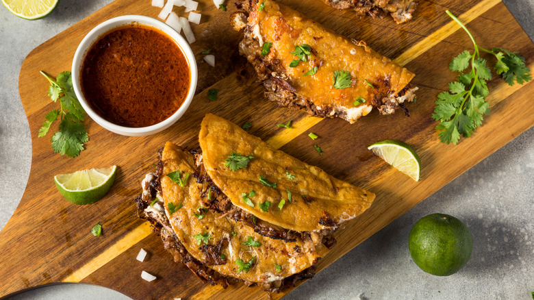 Several birria tacos on a wooden cutting board with consommé
