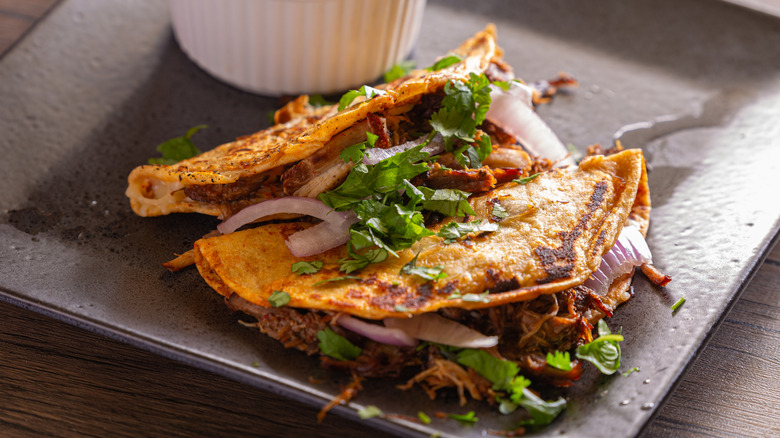 Two birria tacos garnished with onions and cilantro