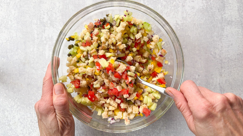 Mixing panzanella salad in glass bowl with spoon