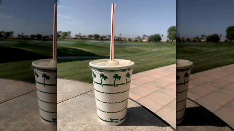 A closeup of a milkshake from In-N-Out with an outdoor landscape in the background