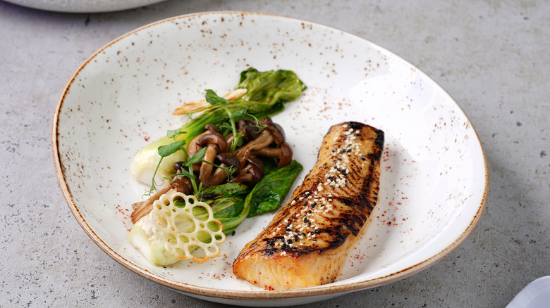 A miso-marinated black cod filet in a bowl with a salad.