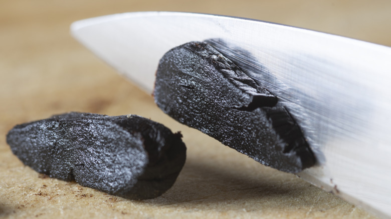A knife slicing through black garlic.