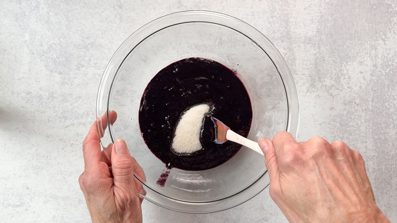 Stirring sugar into blackberry puree in glass bowl with spatula