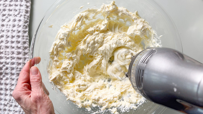 Beating together cream cheese and mascarpone with hand mixer in glass bowl