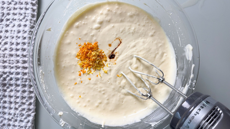 Adding vanilla extract, orange and lemon zest to cheesecake batter in glass bowl with hand mixer