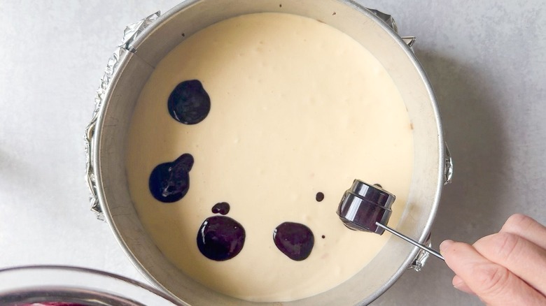 Adding tablespoons of blackberry puree to cheesecake batter in springform pan