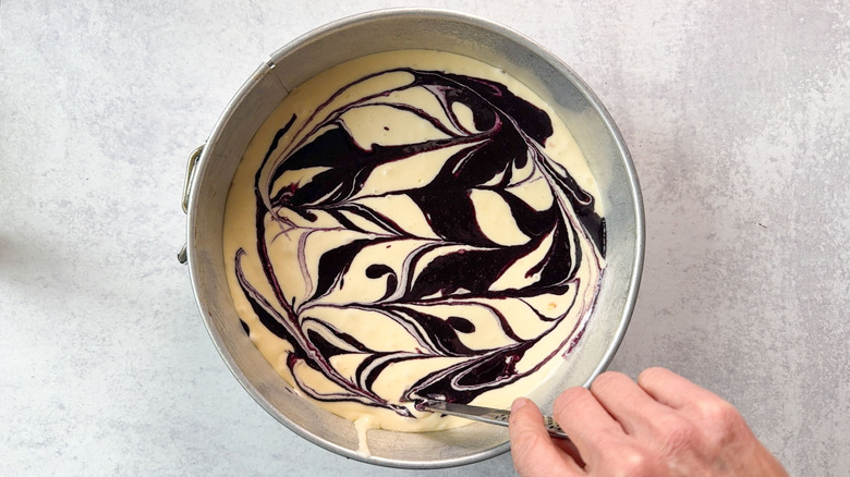 Marbling blackberry puree into cheesecake batter in springform pan with a knife