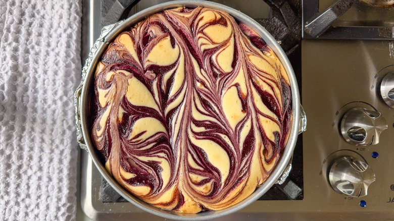 Marbled blackberry cheesecake cooling on stovetop in springform pan