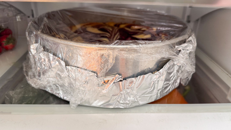 Blackberry cheesecake in springform pan wrapped with foil and plastic in refrigerator