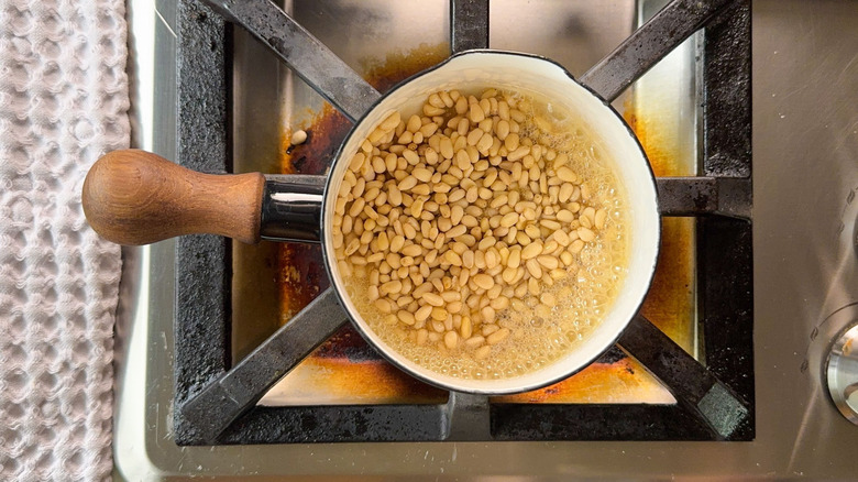 Sugar syrup and pine nuts cooking in saucepan on stovetop