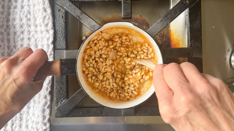 Stirring pine nuts in caramel syrup with wooden spoon in saucepan on stovetop