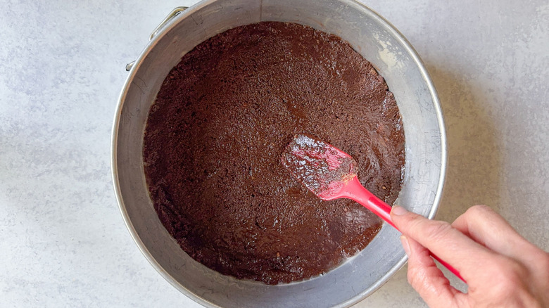 Pressing chocolate graham cracker crust into springform pan with rubber spatula