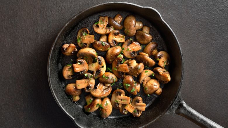 Crimini mushrooms being sauteed in a cast iron pan with herbs.