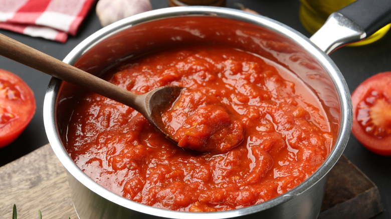 A pot of tomato sauce on a wooden board with a wooden spoon.