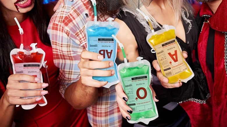 People's hands are seen holding colorful drinks served in novelty IV bags