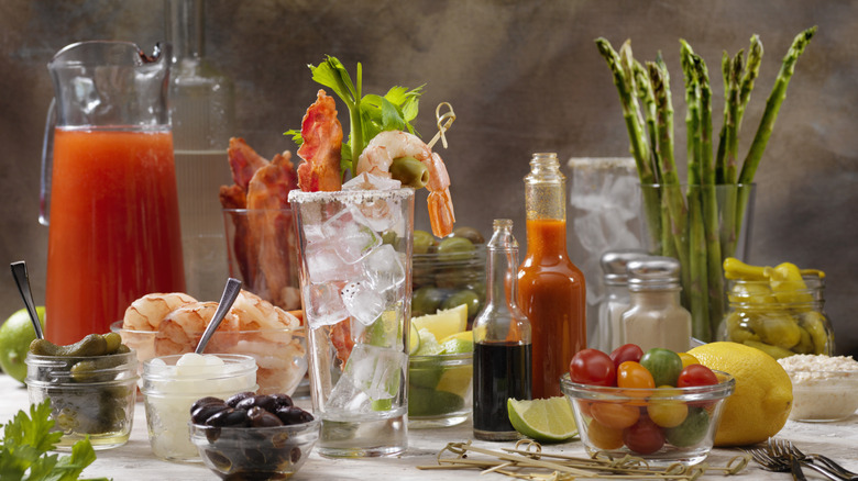 Abundant bloody Mary ingredients including tomato juice, olives, lemon, and extras like shrimp and asparagus.