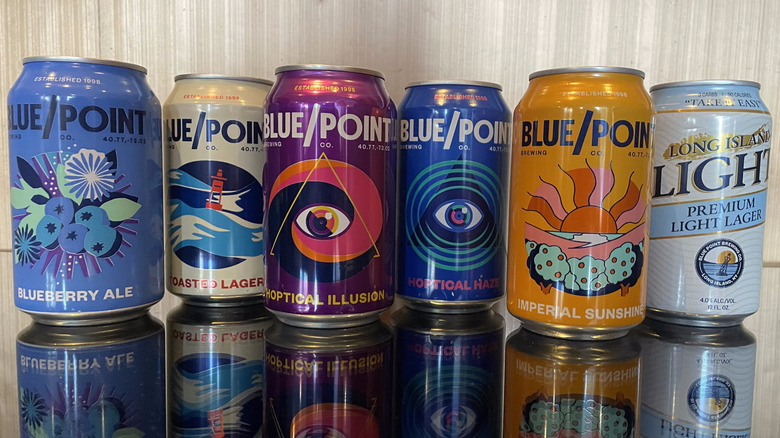 All six Blue Point beers sit in a staggered line on a reflective surface.