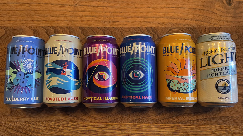 All six Blue Point beers lying down on a table top in a row.