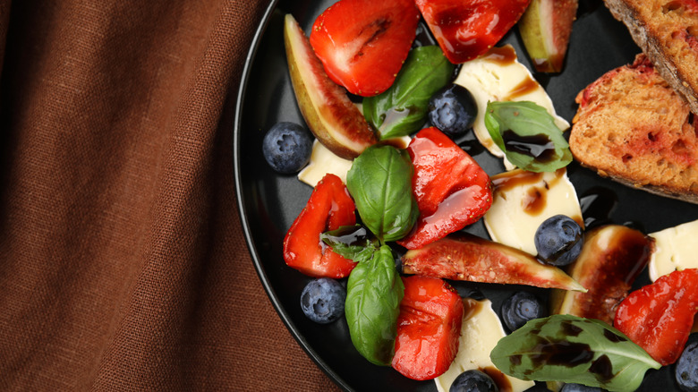 Delicious salad with brie cheese, blueberries, strawberries and balsamic vinegar on table, top view. Space for text