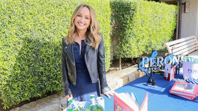 Giada De Laurentiis smiling and standing next to a table of cookbooks