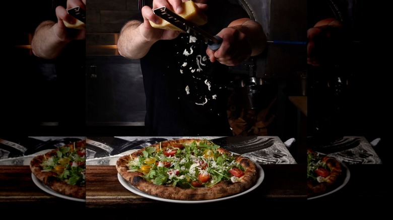 A person's hands are seen shaving Parmesan over a pizza at Razza Pizza Artigianale in Jersey City, New Jersey