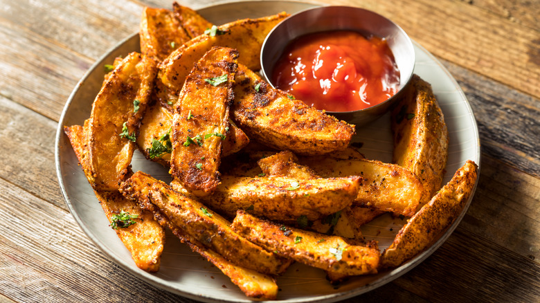 Potato wedges on a beige plate with a ramekin of ketchup and a sprinkle of parsley